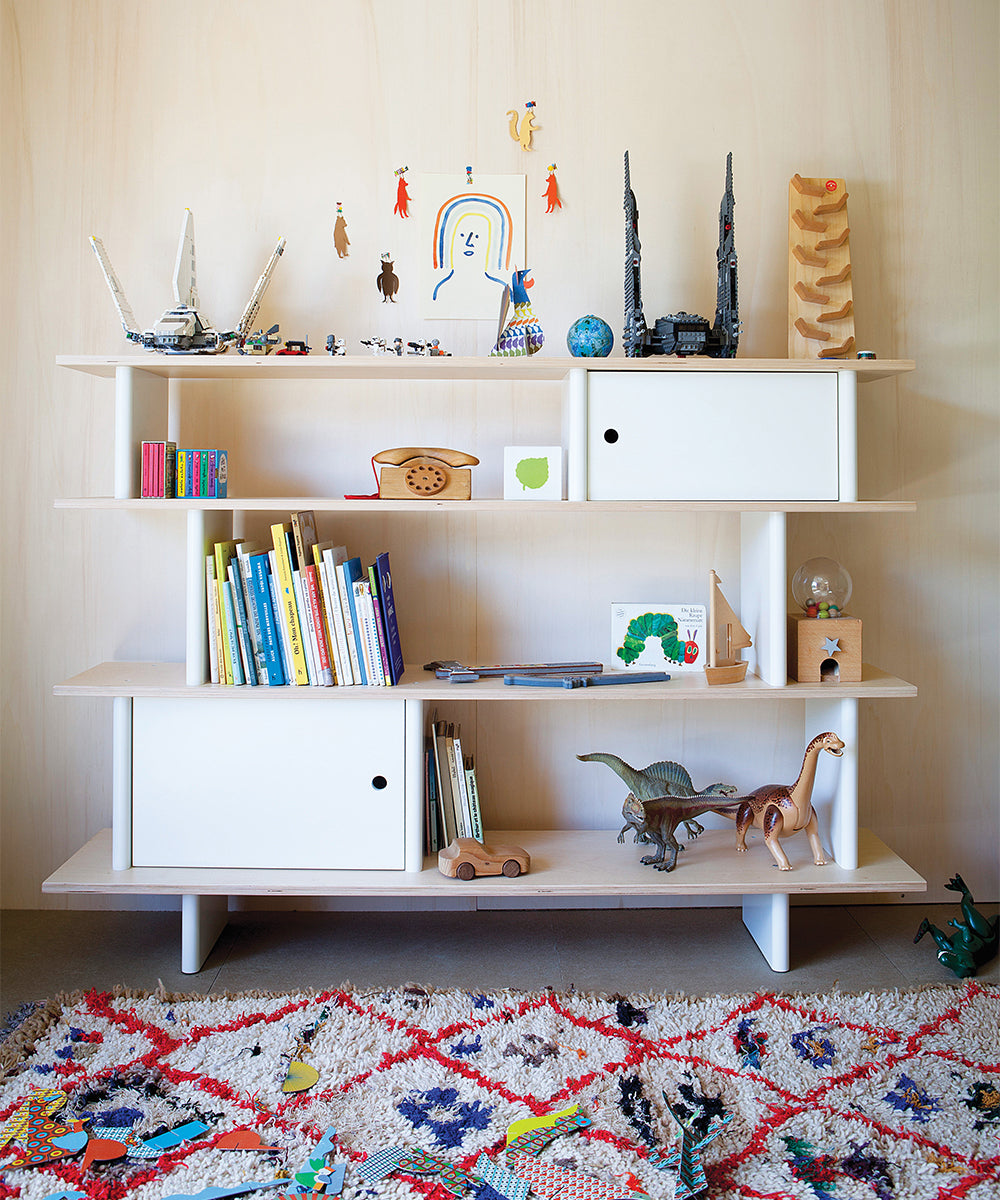 The Mini Library stands on a colorful rug in the playroom, adorned with books, toys, and figurines.