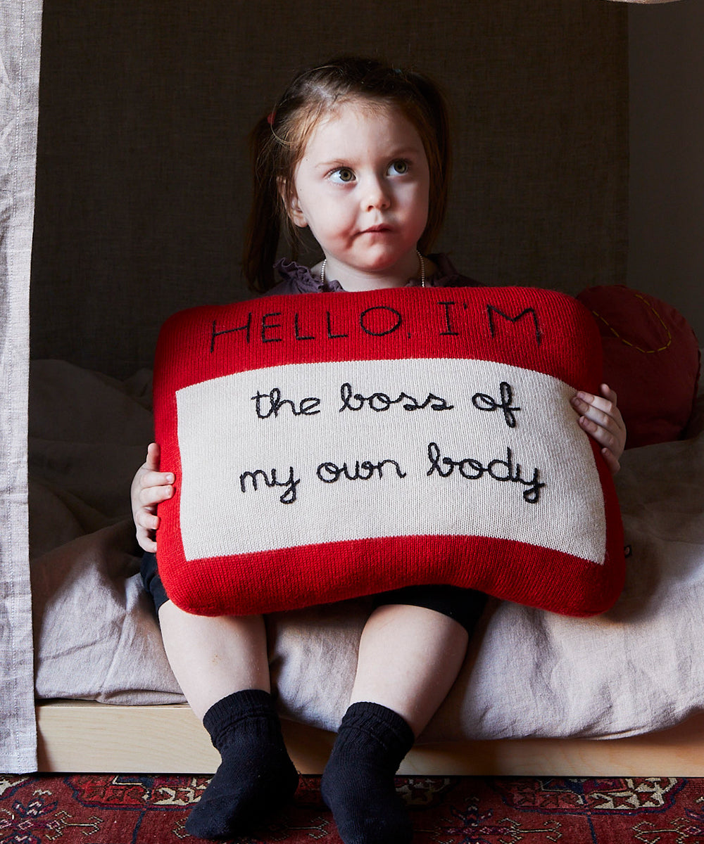 Young girl sitting, holding a Name Tag Pillow that reads "Hello I'm the boss of my own body.