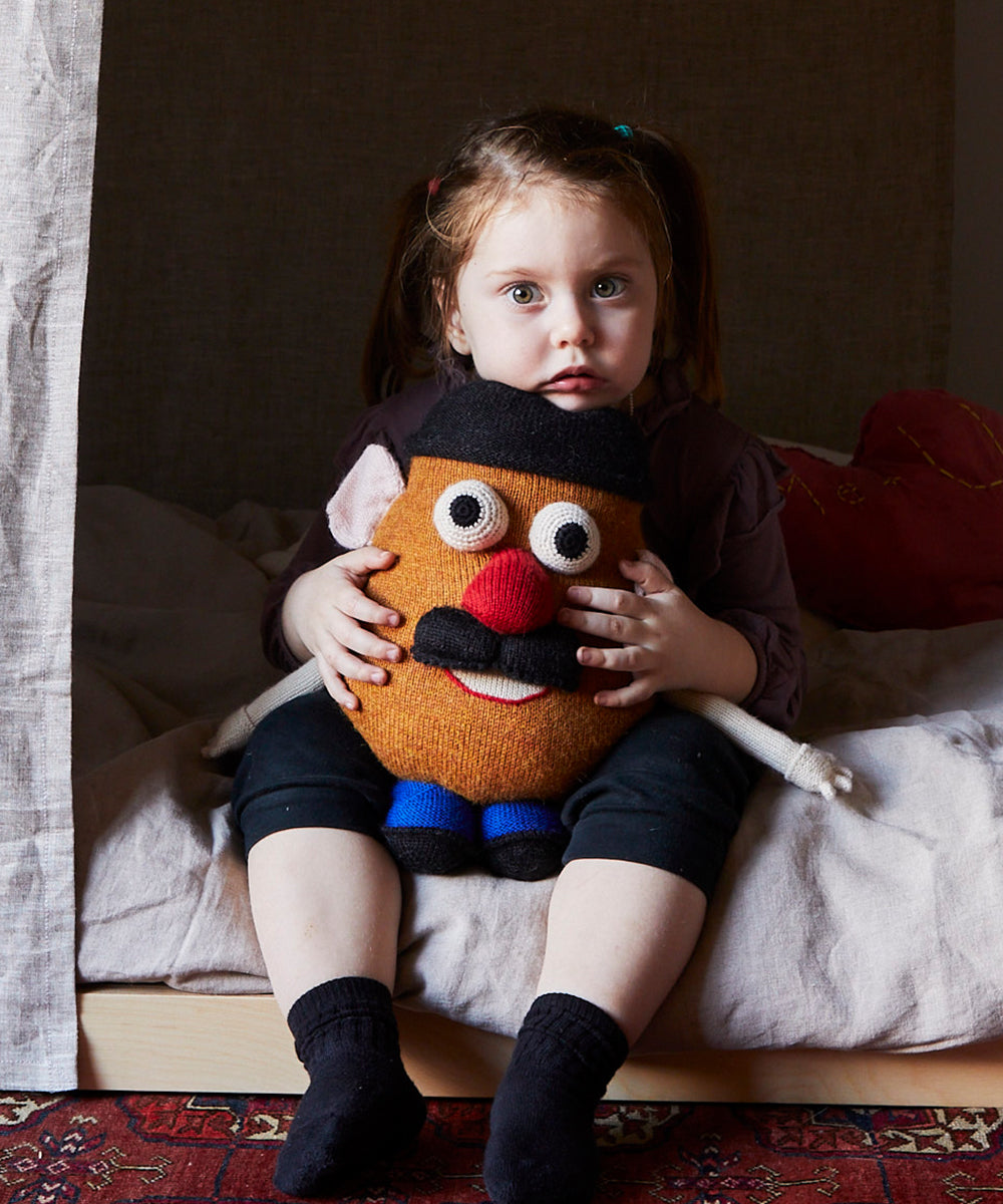 Child sitting on a bed, hugging a Funny Face Pillow, with a solemn expression.