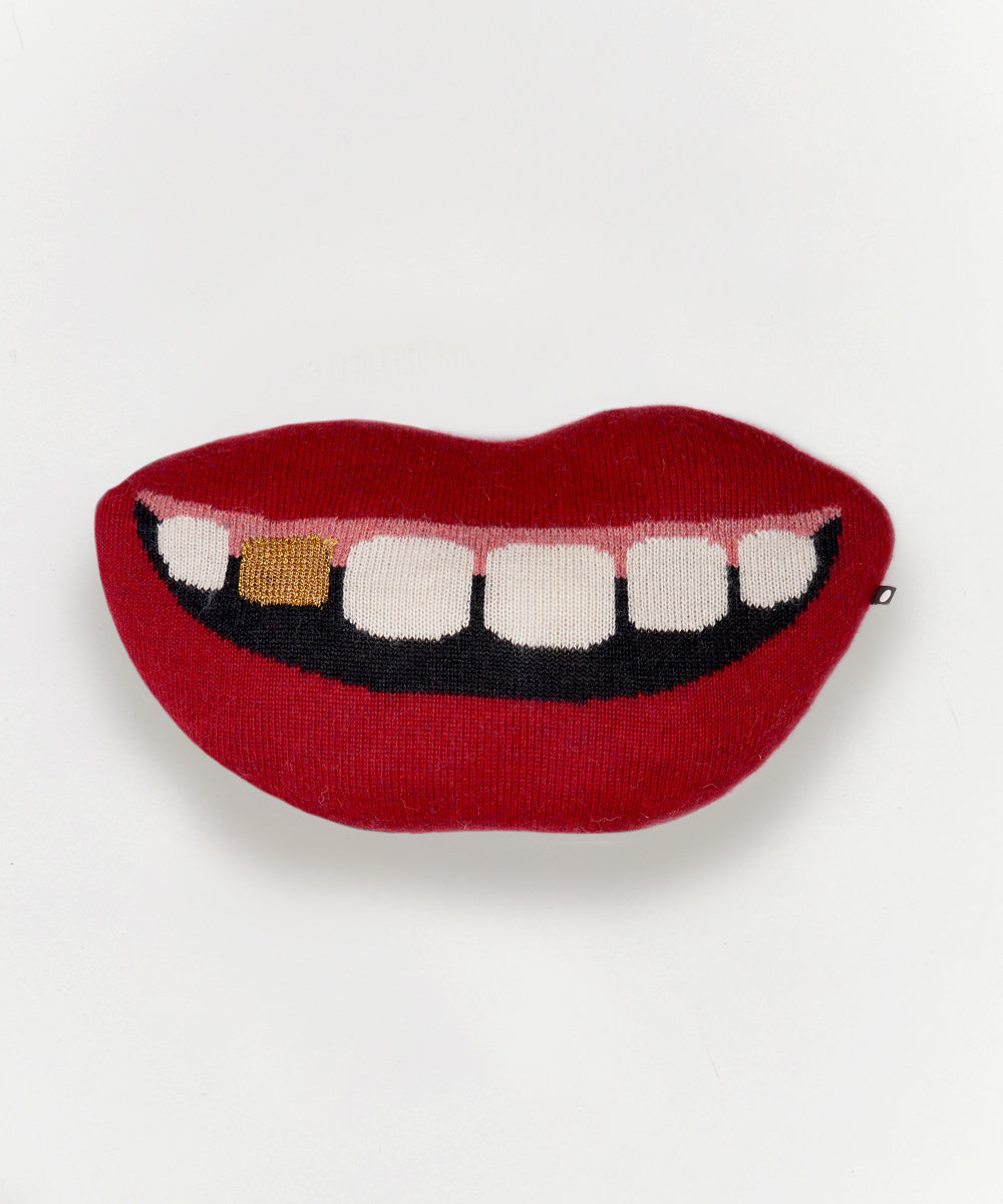 The Mouth Pillow - Gold Tooth is a red, lip-shaped cushion featuring a cartoon smile with white teeth and one gold tooth.