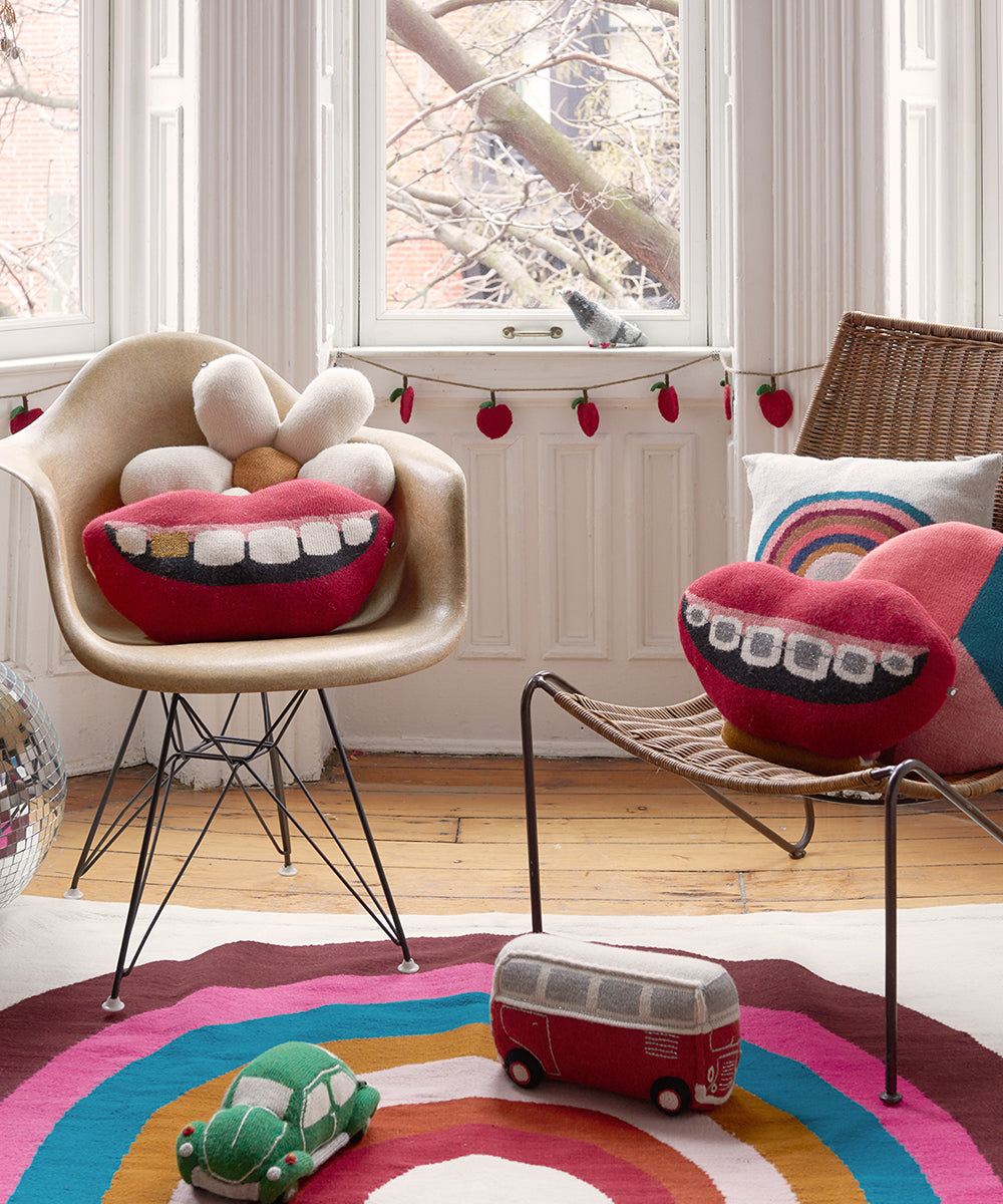 A cozy room with quirky Mouth Pillow - Gold Tooth on chairs, surrounded by colorful decor and toys on a wooden floor.