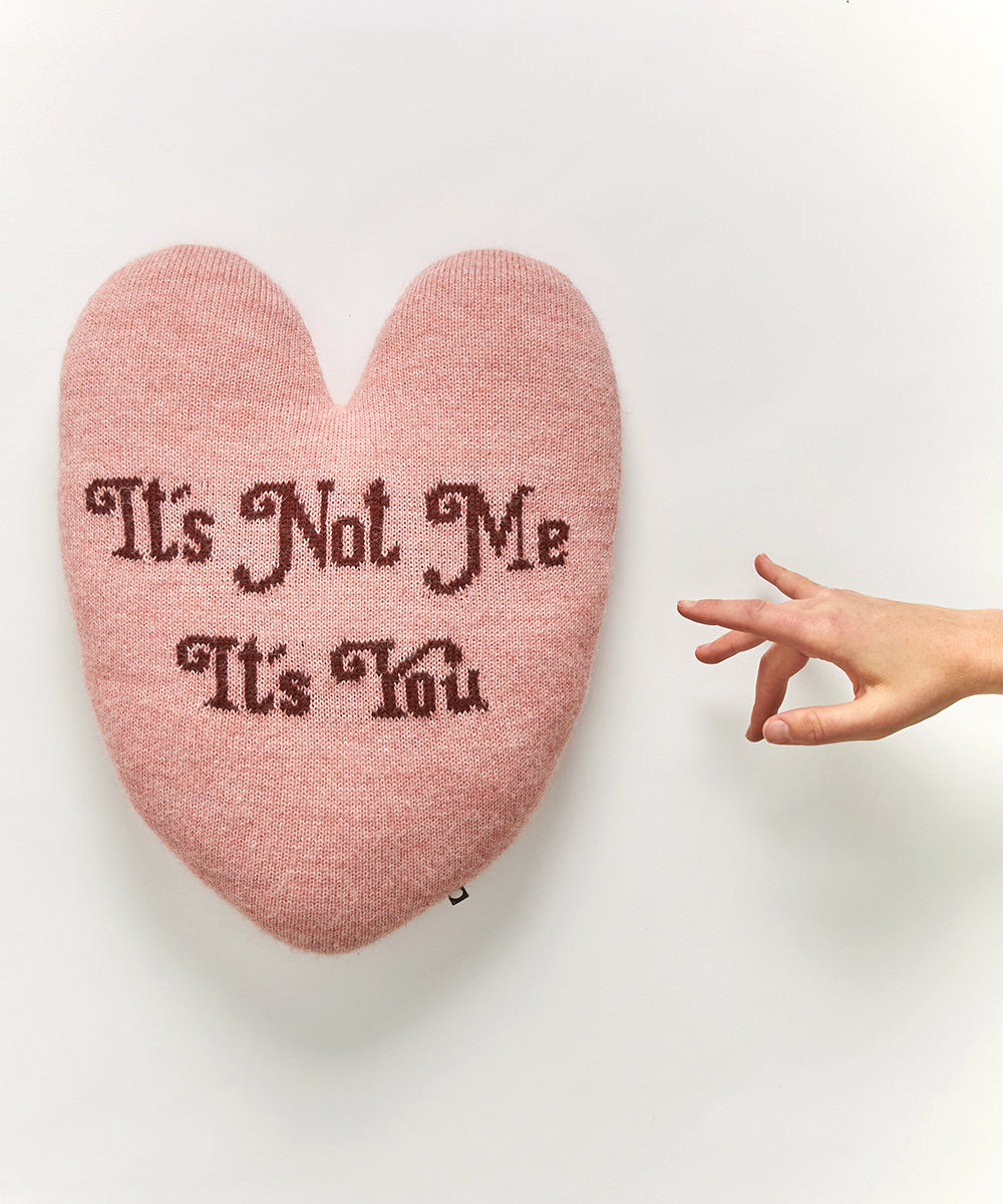 Heart Pillow - It's Not Me, It's You: A pink heart-shaped pillow with hand gesture and text on a plain background.