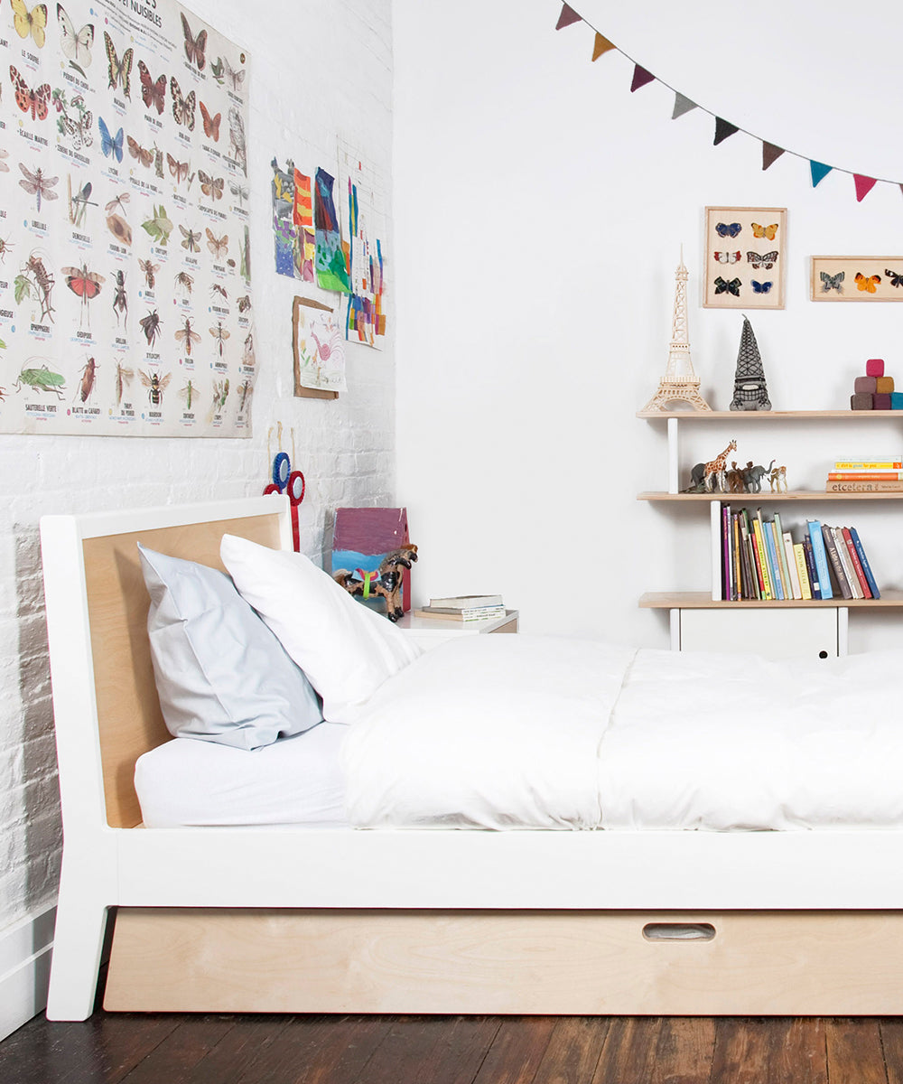 A neatly made Sparrow Twin Bed in a childs room surrounded by books, toys, butterfly posters, and colorful bunting on the walls.